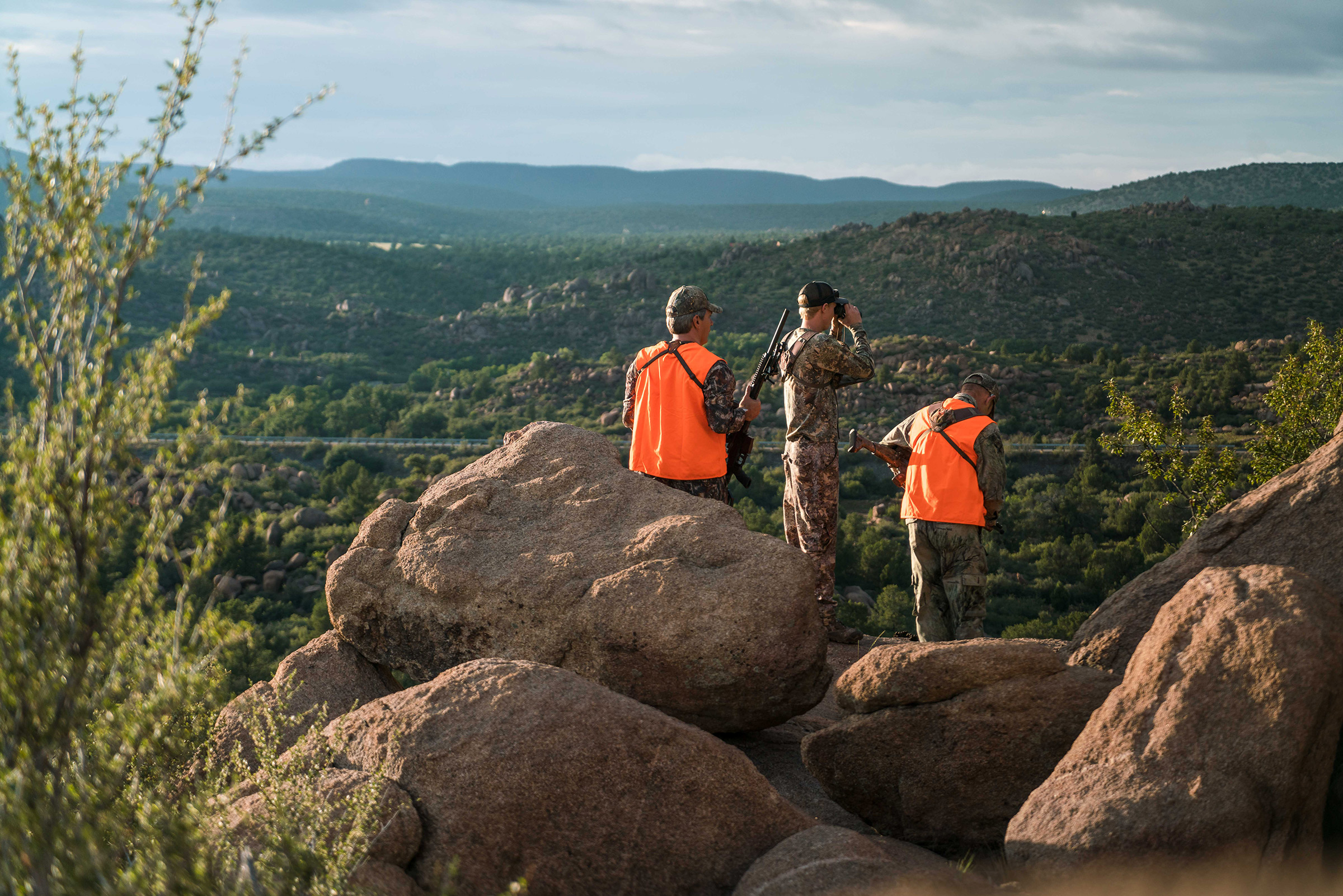 Three hunters on a boulder, holding guns